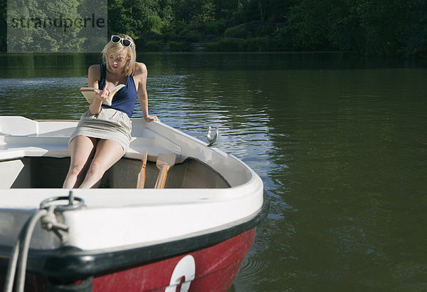 Frau liest Buch auf dem Ruderboot