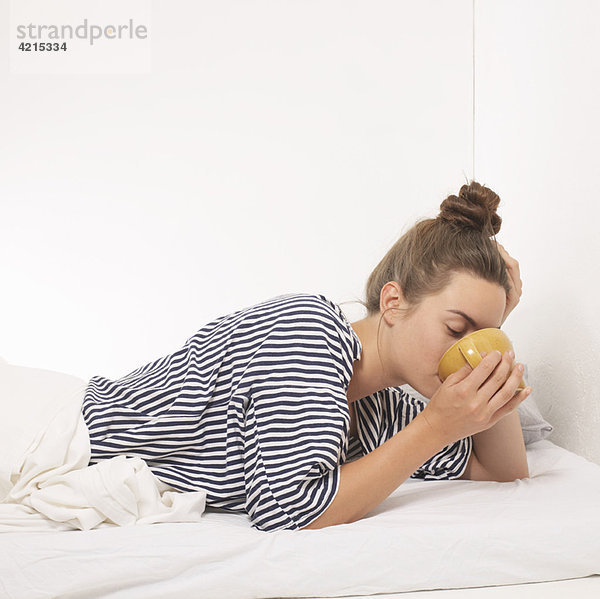 Frau im Bett trinkt aus der Tasse