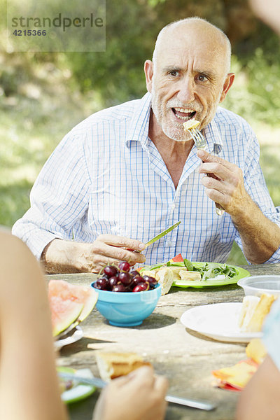 Älterer Mann beim Essen am Picknicktisch