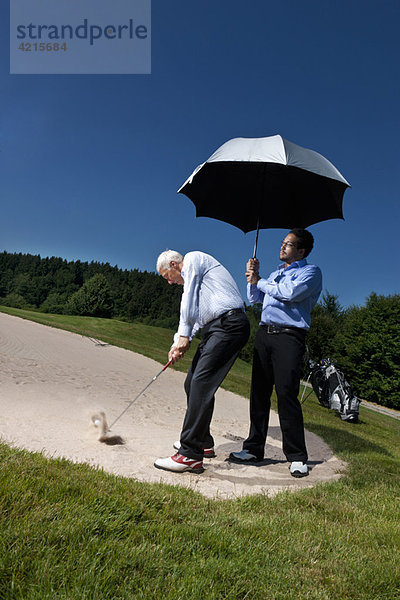 Caddy hält einen Sonnenschirm über einem Golfer.