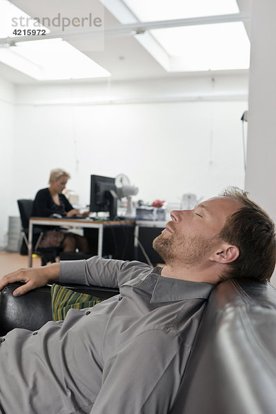 Mann schläft auf dem Sofa im Büro