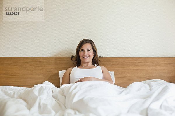 Glückliche Frau im Bett sitzend