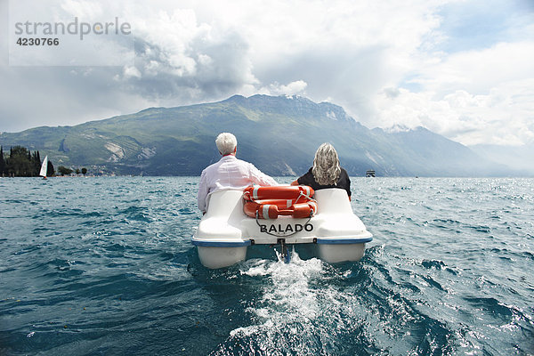 Seniorenpaar mit Tretboot vor Berglandschaft  Italien  Riva del Garda  Gardasee