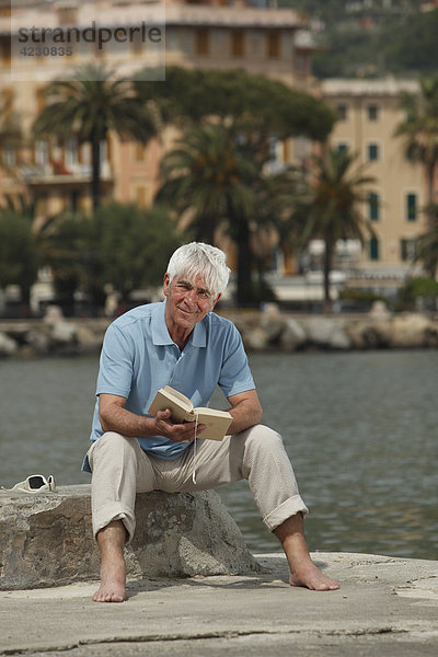 Senior sitzt mit Buch am Wasser  Italien  Rapallo