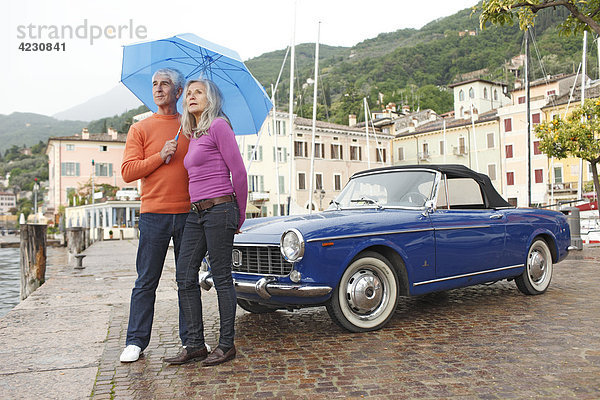 Seniorenpaar mit Oldtimer und Regenschirm am Hafen  Italien  Gargnano  Gardasee