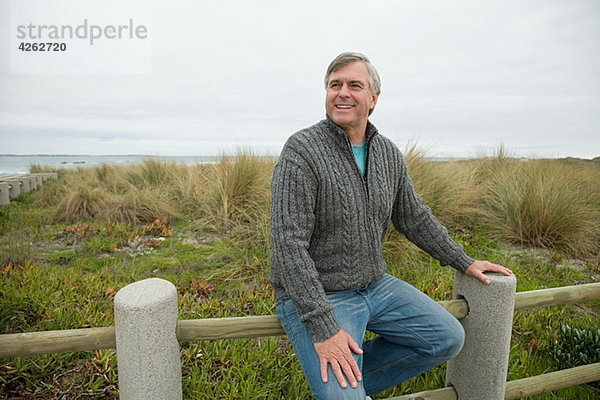 Mann auf einem Zaun an der Küste sitzend