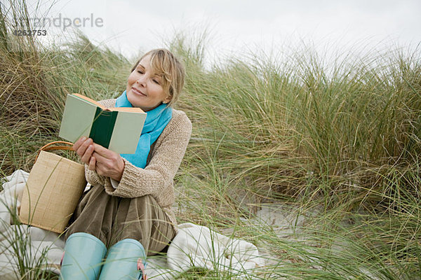 Frau beim Lesen eines Buches auf einer Düne