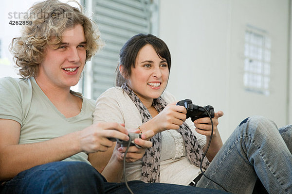 Teenager-Pärchen beim Spielen mit Spielkonsolen