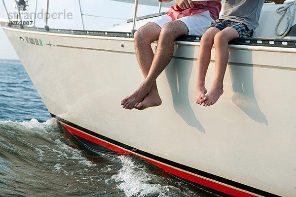 Vater und Sohn auf der Yacht sitzend  Beine baumelnd