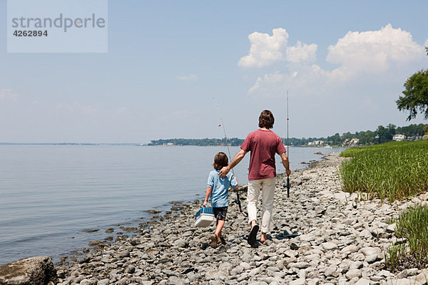 Vater und Sohn gehen mit Angelruten am Strand entlang.