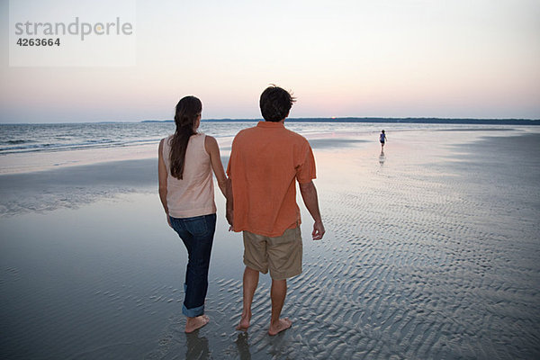 Paar Wandern am Strand mit Tochter in Entfernung