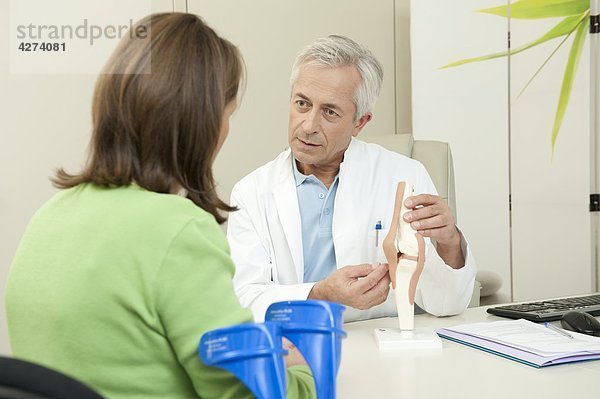 Arzt zeigt einer Patientin ein künstliches Kniegelenk