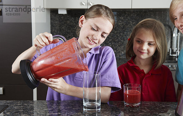 Girls gießen Fruchtsaft aus dem Mixer