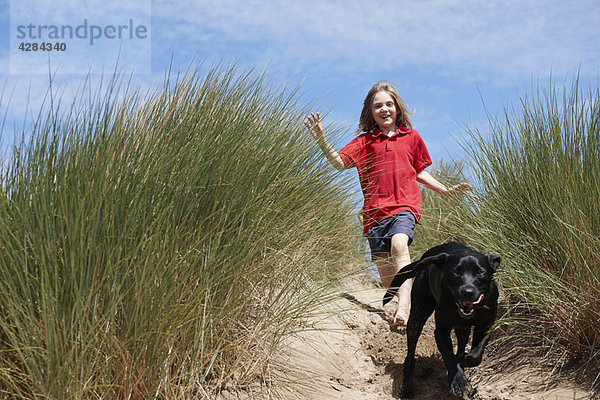 Junges Mädchen jagt Hund in Sanddünen