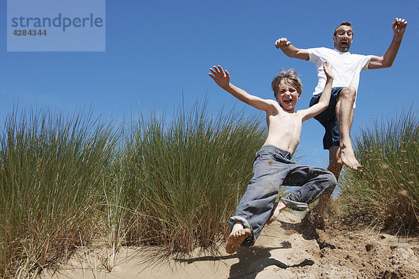 Vater und Sohn springen in Sanddünen