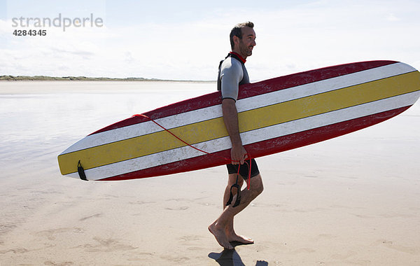 Männlicher Surfer mit Brett am Strand