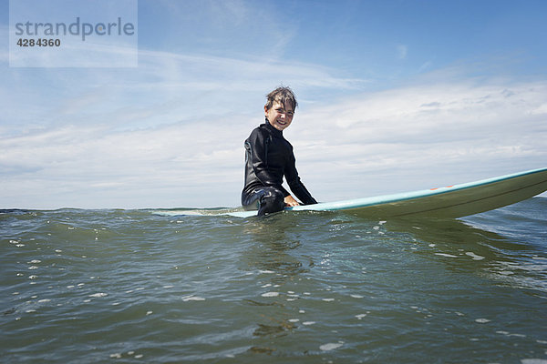 Kleiner Junge sitzt auf dem Surfbrett auf dem Meer