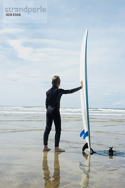 Junge mit Blick aufs Meer mit Surfbrett