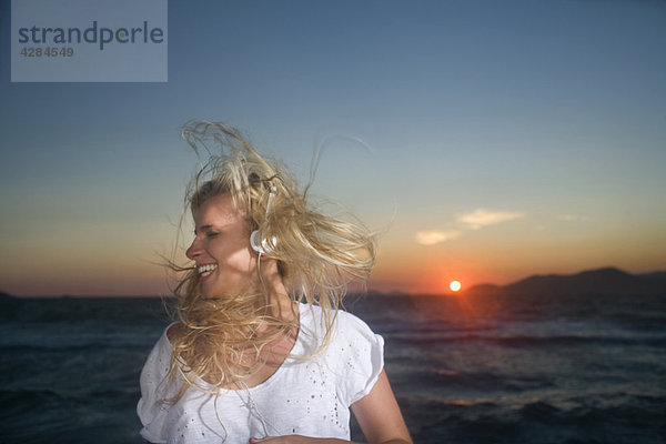 Junge Frau trägt bei Sonnenuntergang Ohrhörer