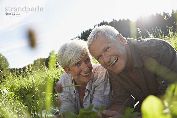 Seniorenpaar lächelnd auf den Wiesen liegend