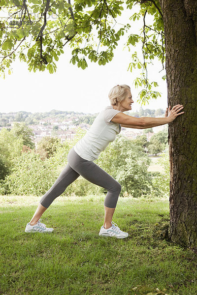 Frau streckt Bein am Baum festhaltend aus