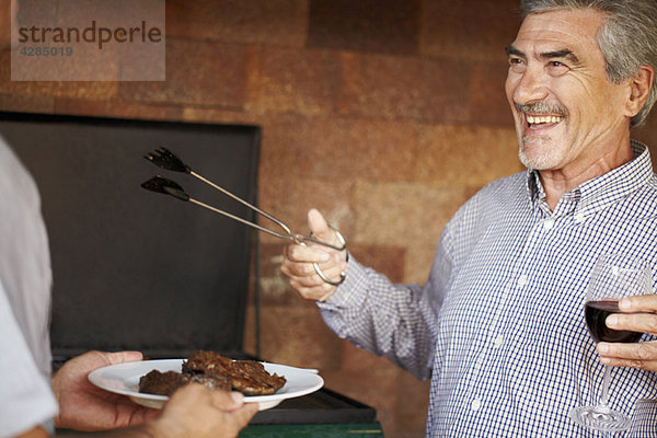 Glücklicher älterer Mann serviert Fleisch vom BBQ