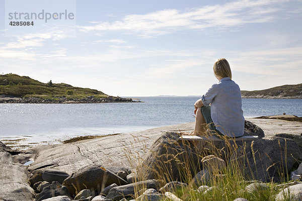 Frau sitzend und mit Blick aufs Meer