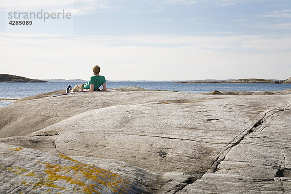 Auf Felsen liegender Mann mit Blick aufs Meer