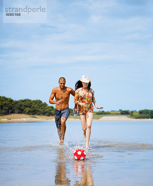 Paar spielt Fußball am Strand