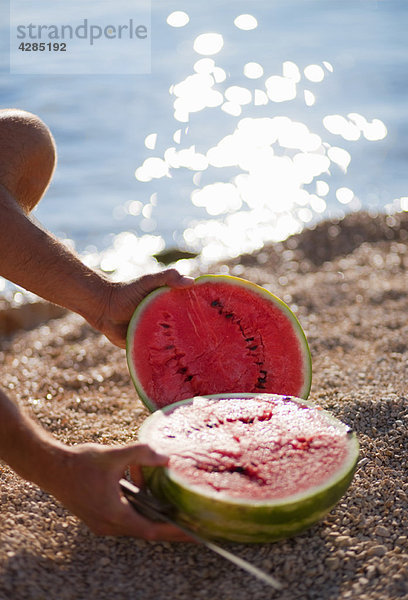 Mann schneidet Wassermelone am Strand