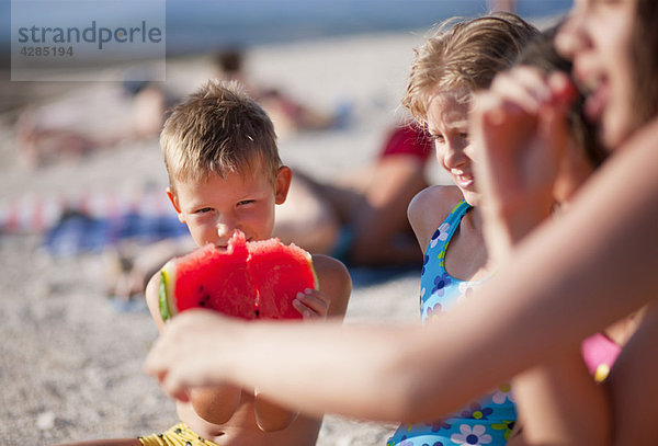 Kinder essen Wassermelone am Strand