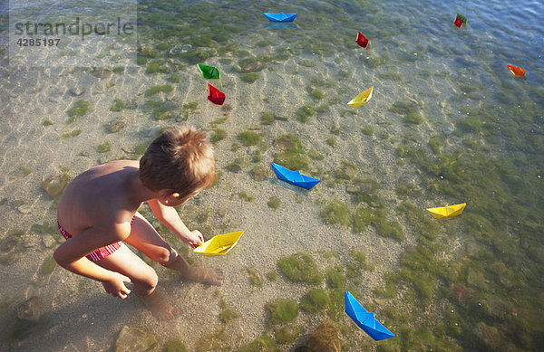 Junge schwimmende Papierboote am Strand