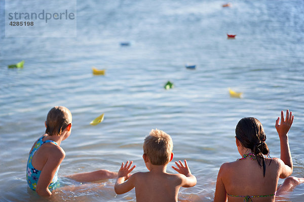 Kinder schwimmende Papierboote am Strand