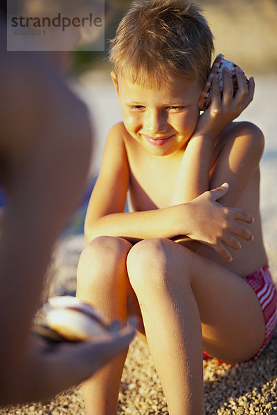 Junge hört Muscheln am Strand