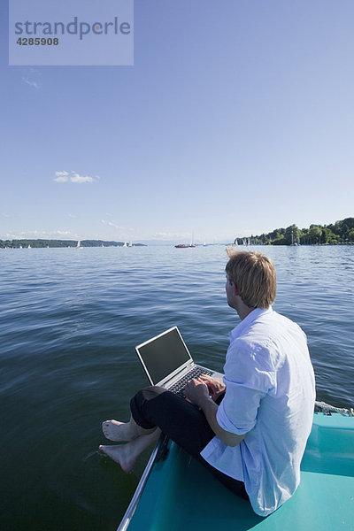 Mann sitzend mit Laptop am See