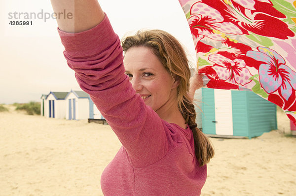 Glückliche Frauen am Strand halten Handtuch im Wind