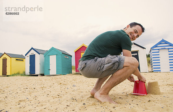 Glücklicher Mann macht Sandburgen am Strand