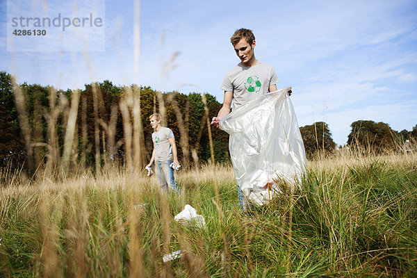 Junger Mann sammelt Müll in der Natur auf