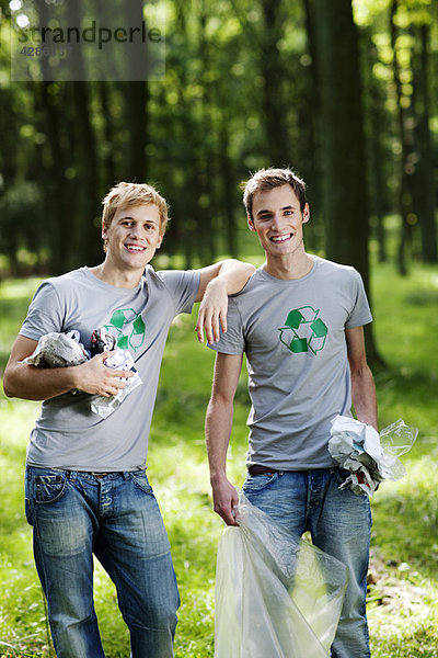 Zwei junge Männer sammeln Müll im Wald.