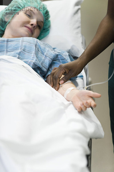 Der Patient beobachtet  wie die Krankenschwester die Platzierung der IV-Nadel im Arm kontrolliert.