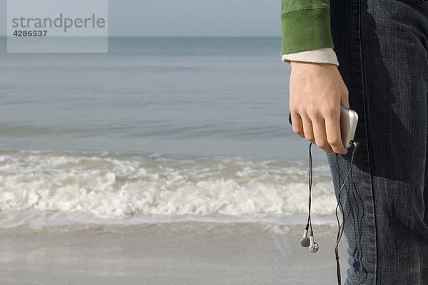 Person am Strand stehend  MP3-Player in der Hand  beschnitten