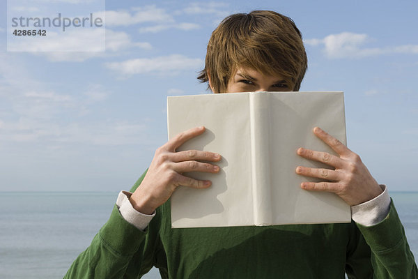 Junger Mann hält Buch vor dem Gesicht  Porträt