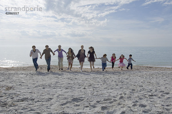 Gruppe von Menschen  die sich an den Händen halten und gemeinsam am Strand rennen.