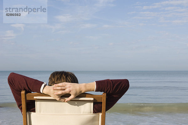 Junger Mann entspannt im Stuhl am Strand  Rückansicht