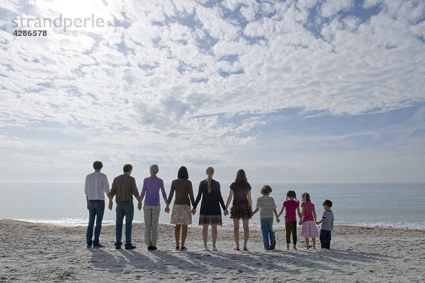 Gruppe von Menschen  die am Strand stehen und Händchen halten.