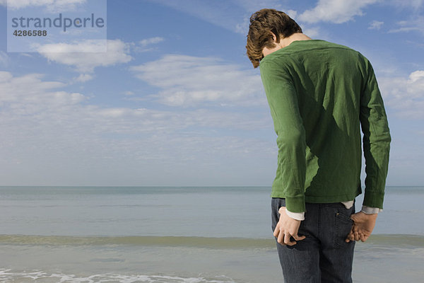 Junger Mann am Strand stehend mit Kopf nach unten  Rückansicht