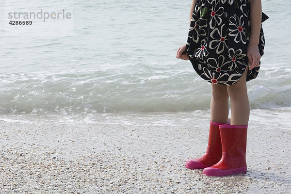 Mädchen am Strand stehend  mit Gummistiefeln