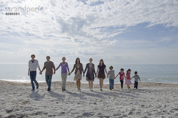Gruppe von Menschen  die sich an den Händen halten und gemeinsam am Strand spazieren gehen.