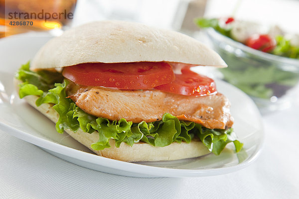 Chicken Sandwich auf weiße Platte  geringe Tiefenschärfe auf Salat und Getränk auf Tischplatte
