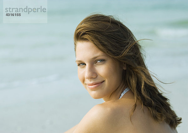 Junge Frau am Strand  über die Schulter lächelnd vor der Kamera